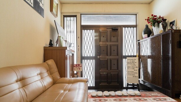 A living room with a beige sofa, a wooden cabinet, and a door with a sign. - Private bedroom in a shared English-speaking house (大阪市)