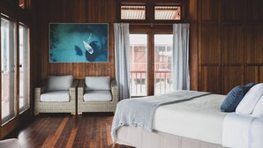A room with a large bed, two wicker chairs, a wooden ceiling, and a large window with curtains. - Camp Island Lodge (Camp Island)