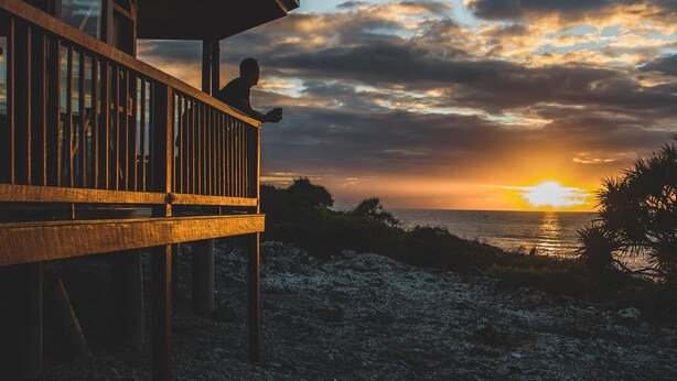 A wooden balcony overlooking a sunset with a view of the ocean. - Camp Island Lodge (Camp Island)