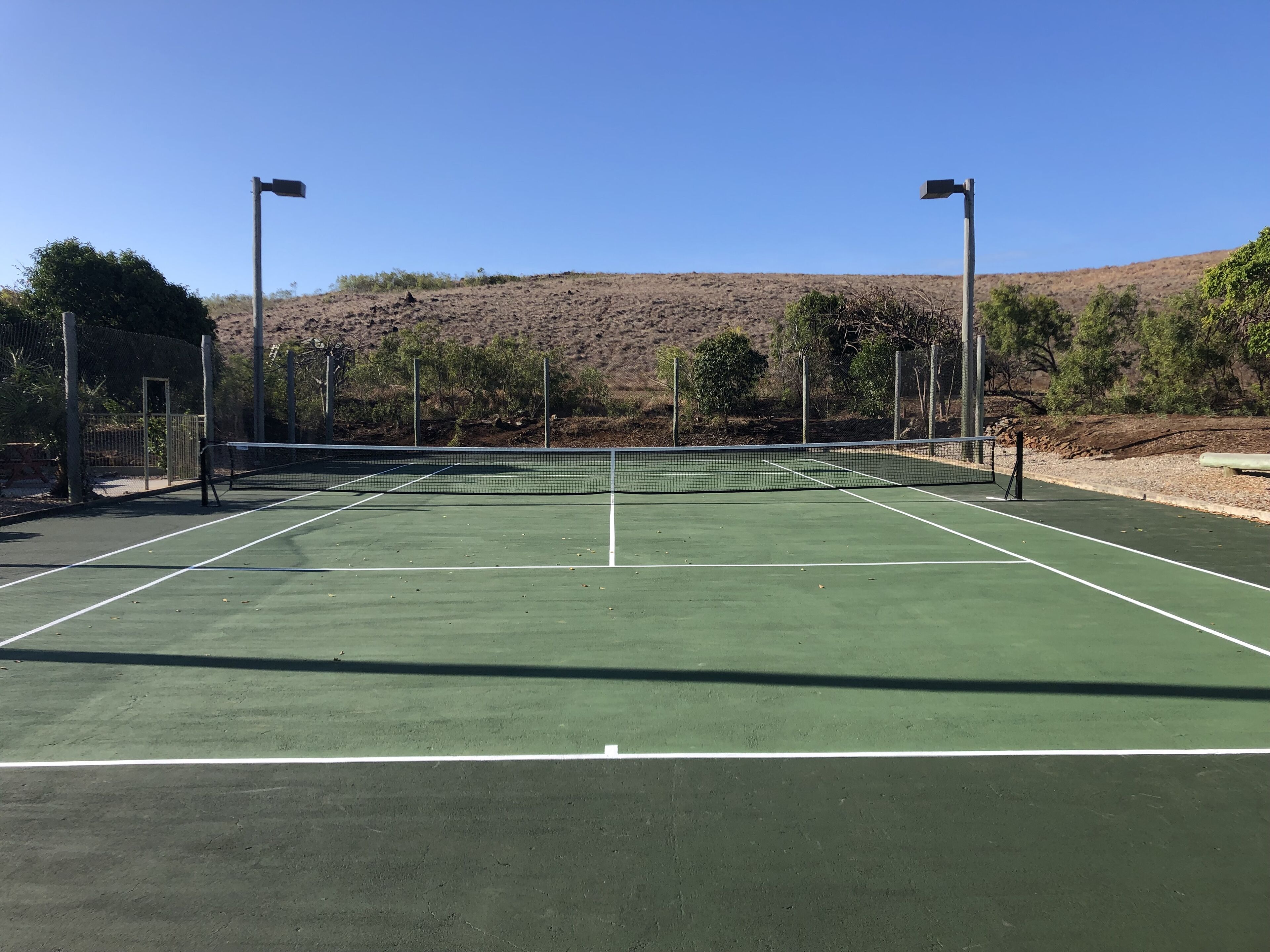 Un campo da tennis con una rete, circondato da una recinzione, e una collina sullo sfondo.