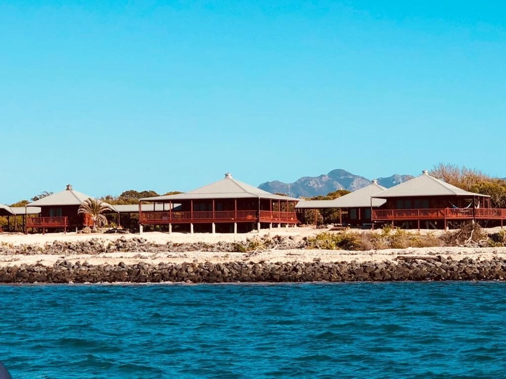 A beachfront property with multiple buildings, a rocky shoreline, and mountains in the background.