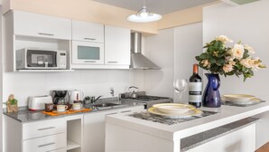 A modern kitchen with white cabinetry, a microwave, a stove, and a sink. There is a vase with flowers on the counter, a bottle of wine, and a glass. - DEPTO CENTRO C/PILETA Y VISTA AL LAGO N.HUAPI (San Carlos de Bariloche)