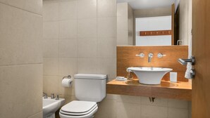 A modern bathroom with a white toilet, a sink, and a mirror above the sink. - DEPTO CENTRO C/PILETA Y VISTA AL LAGO N.HUAPI (San Carlos de Bariloche)