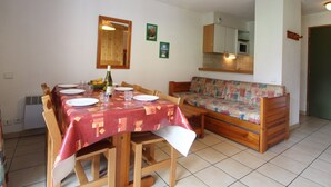 Un coin repas avec une table dressée pour quatre personnes, un banc en bois, un four à micro-ondes et un petit réfrigérateur.