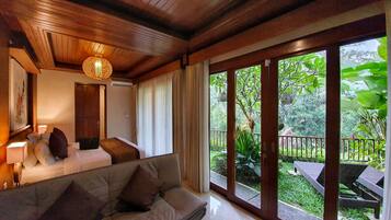 A room with a bed, a sofa, and a large window with a view of a garden.