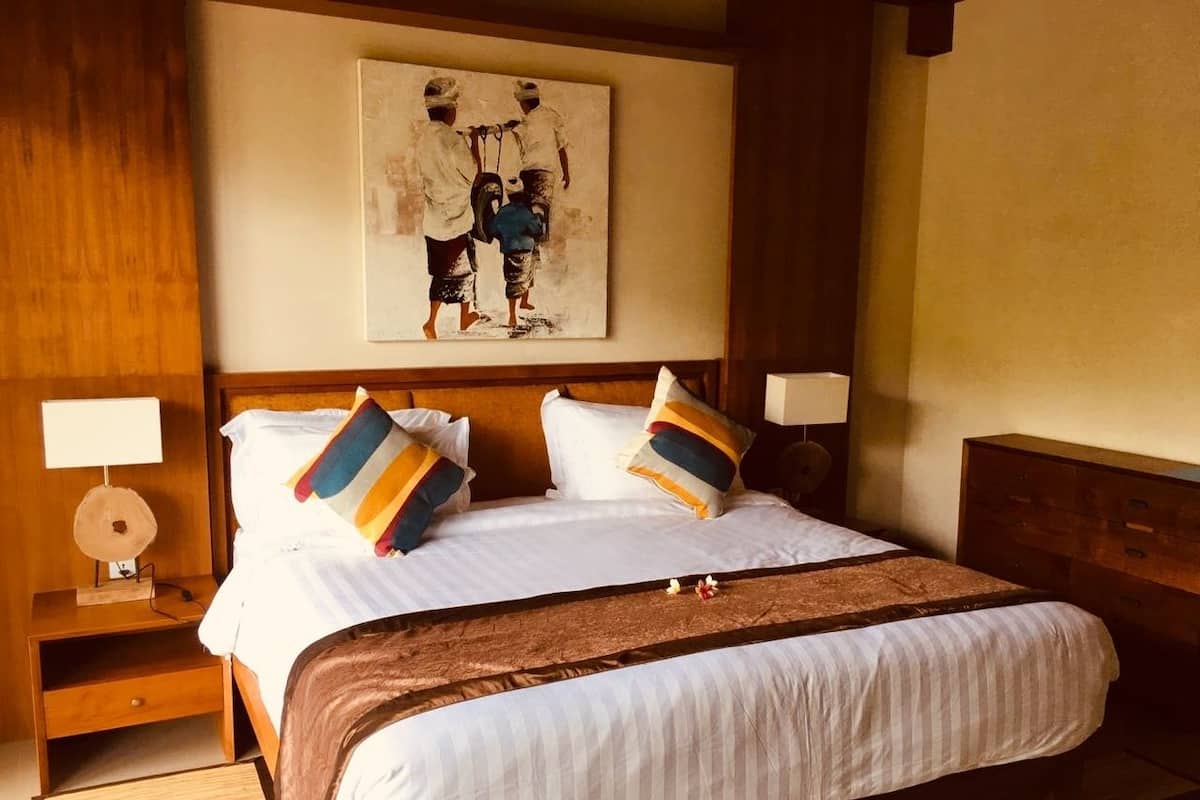 A hotel room with a large bed, two bedside tables, a headboard, and a painting on the wall.