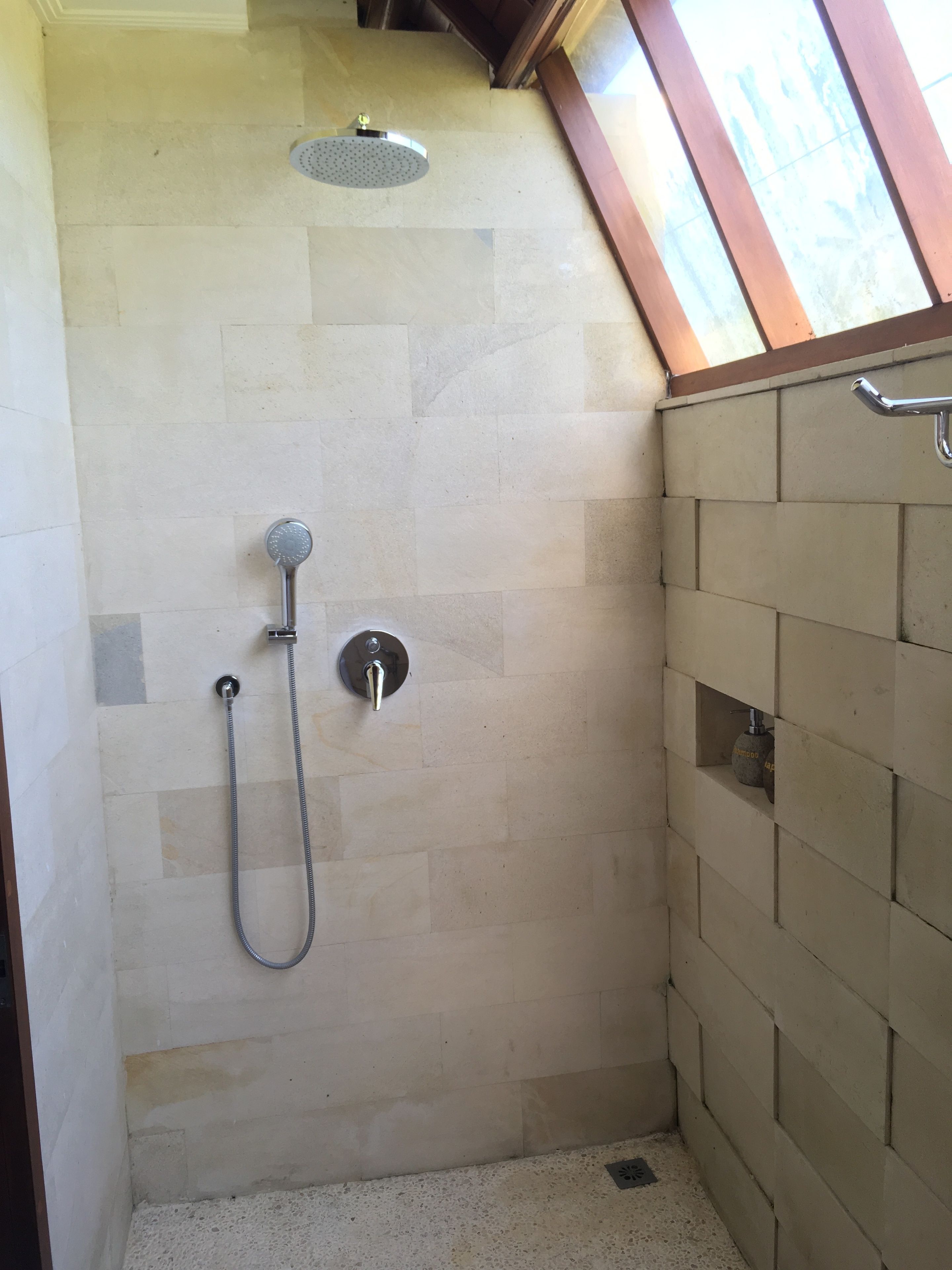 Een douchegedeelte met een betegelde muur, een douchekop en een handdouche.