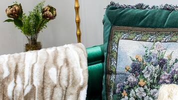 A room with a green sofa, a decorative pillow with a floral design, a brass floor lamp, and a vase with green plants.