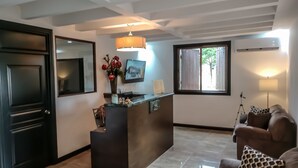 Un moderno vestíbulo de hotel con una recepción, un espejo grande, un jarrón de flores rojas, un televisor montado en la pared y un sofá con cojines estampados.