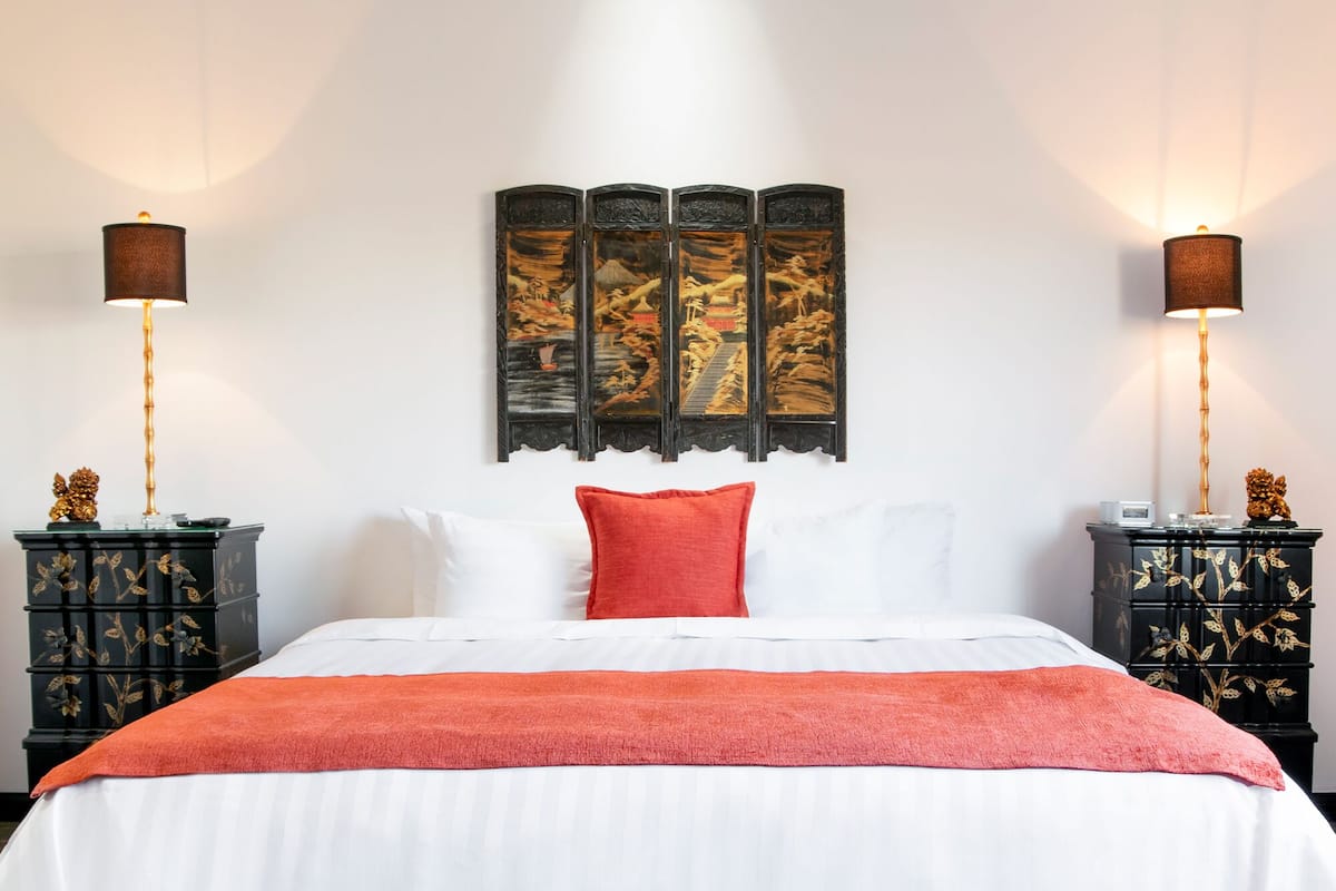 Un lit avec une literie blanche et un plaid rouge, flanqué de deux tables de chevet sur lesquelles sont posées des lampes et des objets décoratifs.