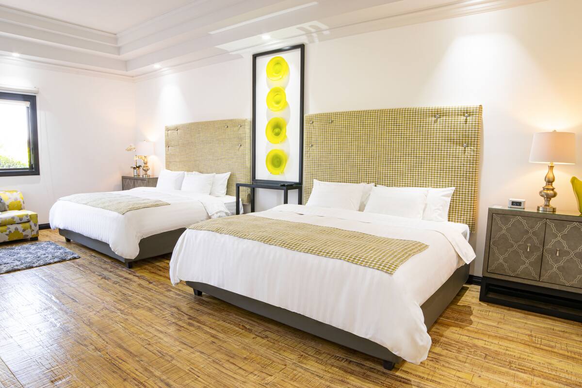 Une chambre d’hôtel avec deux lits, une tête de lit à carreaux, une table de chevet avec une lampe et une grande fenêtre.