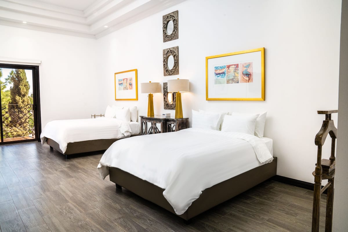 Une chambre d’hôtel avec deux lits, une petite table avec des lampes et des œuvres d’art accrochées aux murs.