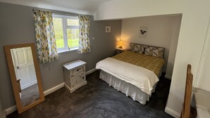 A bedroom with a bed, a nightstand, a dresser, a window with curtains, and a mirror. - The Ship Inn (Gloucester)
