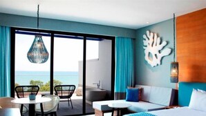A modern hotel room with a large bed, a balcony with a view of the ocean, a seating area with chairs, and a dining table. - Novus Jiva Anyer villa resort and Spa (Banten)