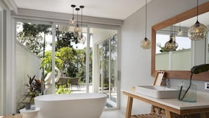 A modern bathroom with a freestanding bathtub, a wooden vanity, and pendant lighting. - Novus Jiva Anyer villa resort and Spa (Banten)