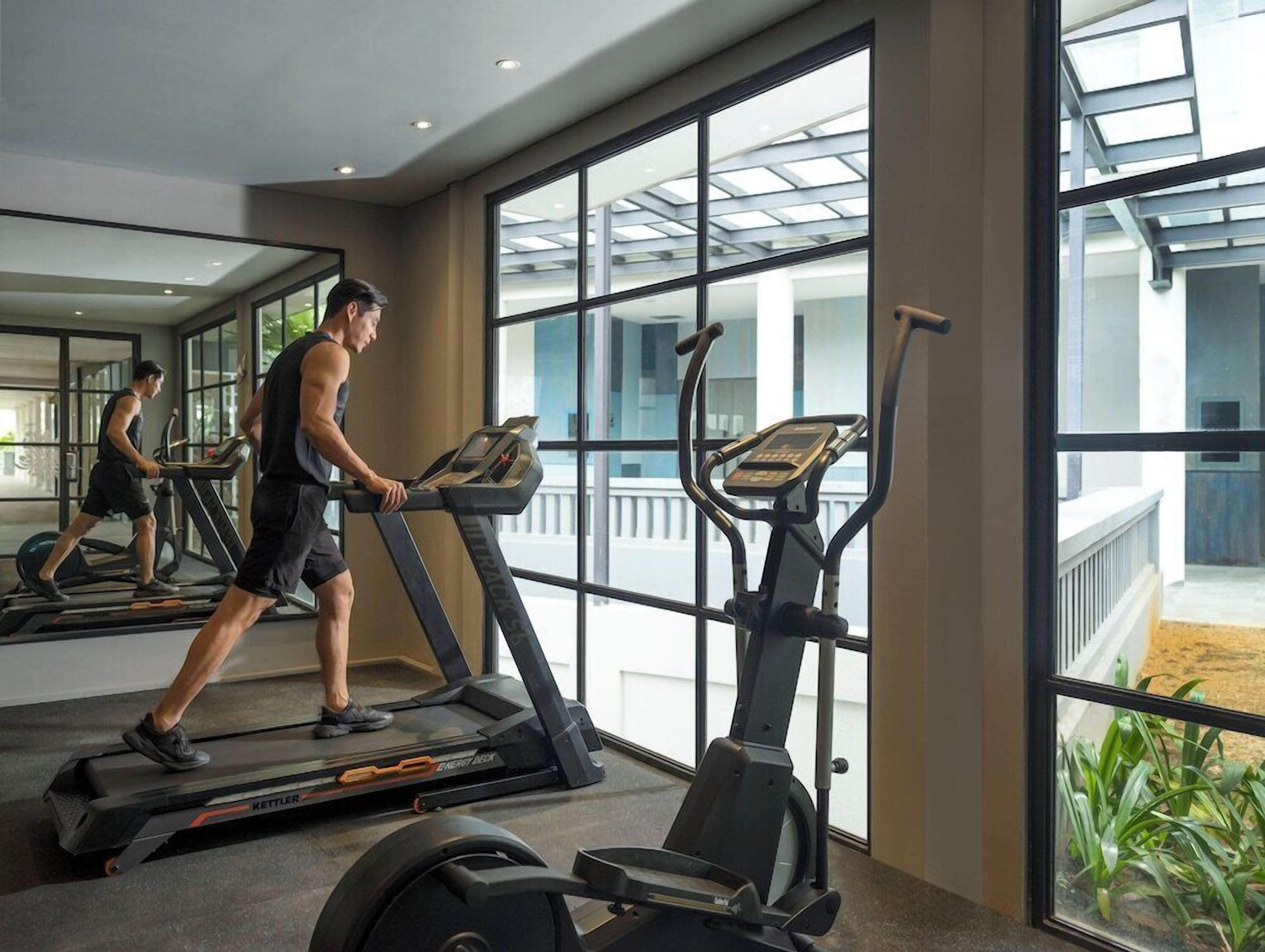 Ein Fitnessraum mit Laufbändern und einem Crosstrainer, großen Fenstern und Blick nach draußen.
