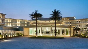 A modern hotel with a circular courtyard, palm trees, and a multi-story building with large windows. - Novus Jiva Anyer villa resort and Spa (Banten)