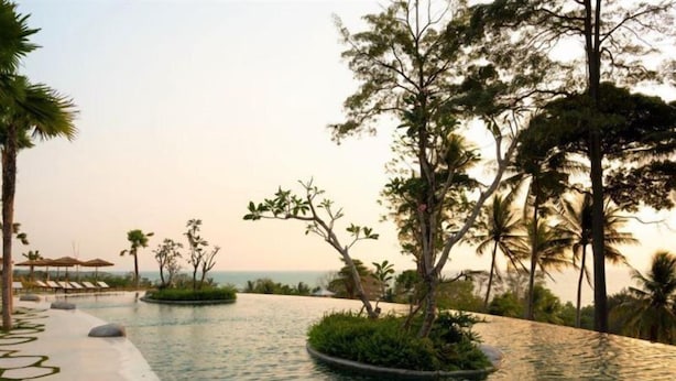 A serene pool area with a curved water feature, surrounded by tropical vegetation and palm trees. - Novus Jiva Anyer villa resort and Spa (Banten)