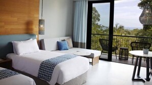 A modern hotel room with a large bed, a sofa, a balcony with outdoor seating, and a view of the outdoors. - Novus Jiva Anyer villa resort and Spa (Banten)