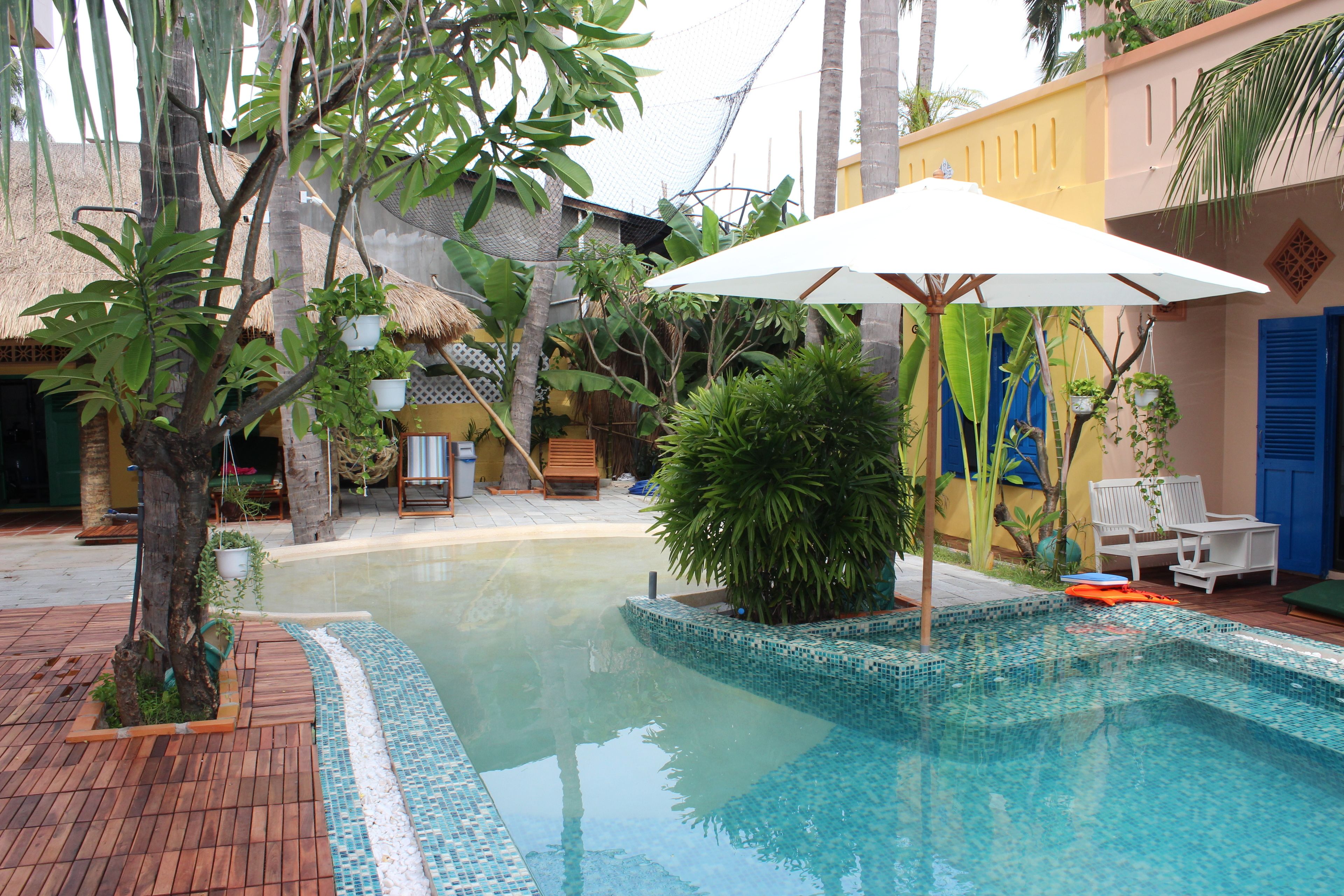 Una piscina con borde de azulejos, rodeada de plantas en macetas y una terraza de madera.