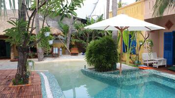 Una piscina con borde de azulejos, rodeada de plantas en macetas y una terraza de madera.