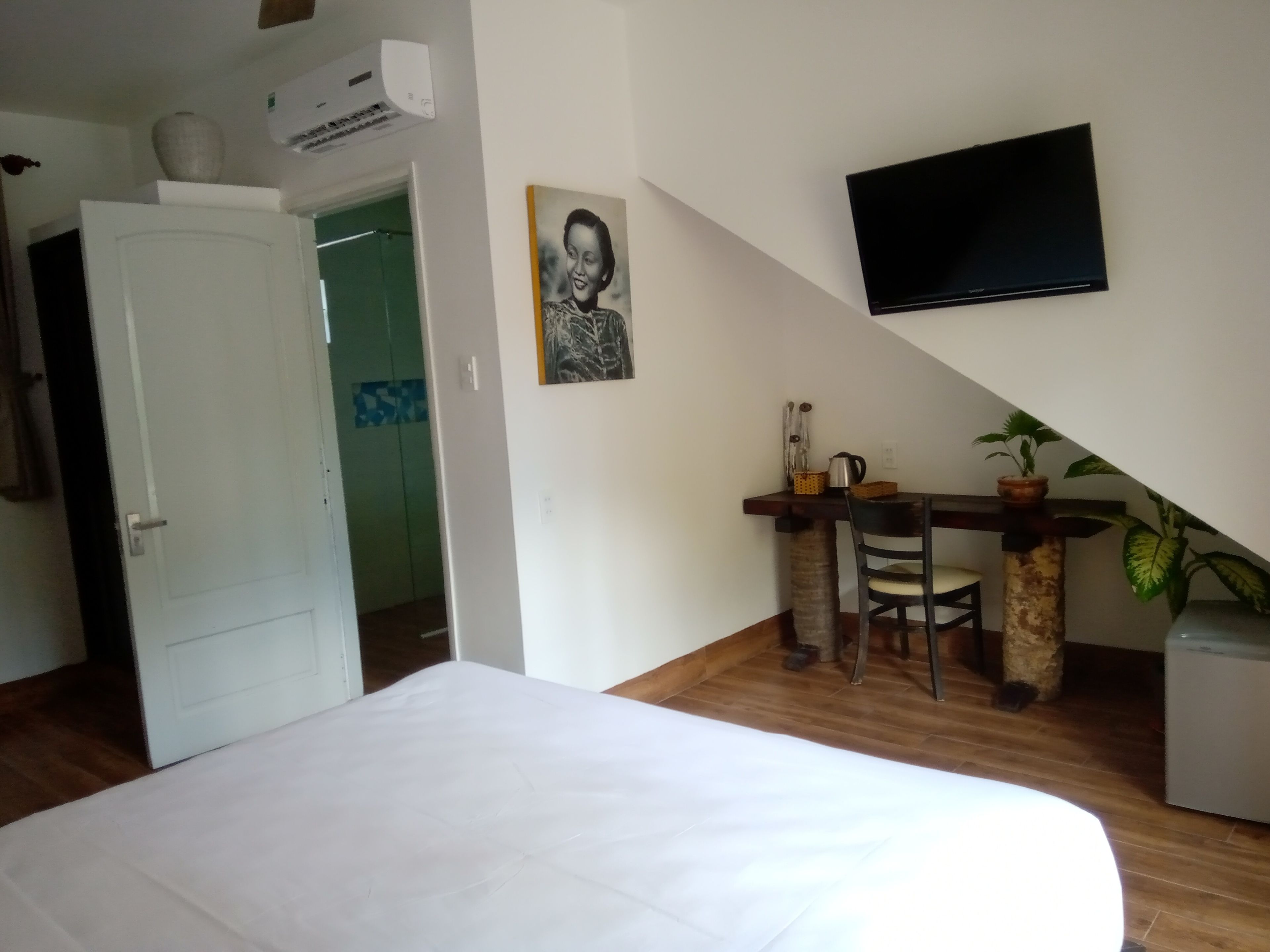Un dormitorio con cama, escritorio y silla, televisor en la pared y una planta en maceta.