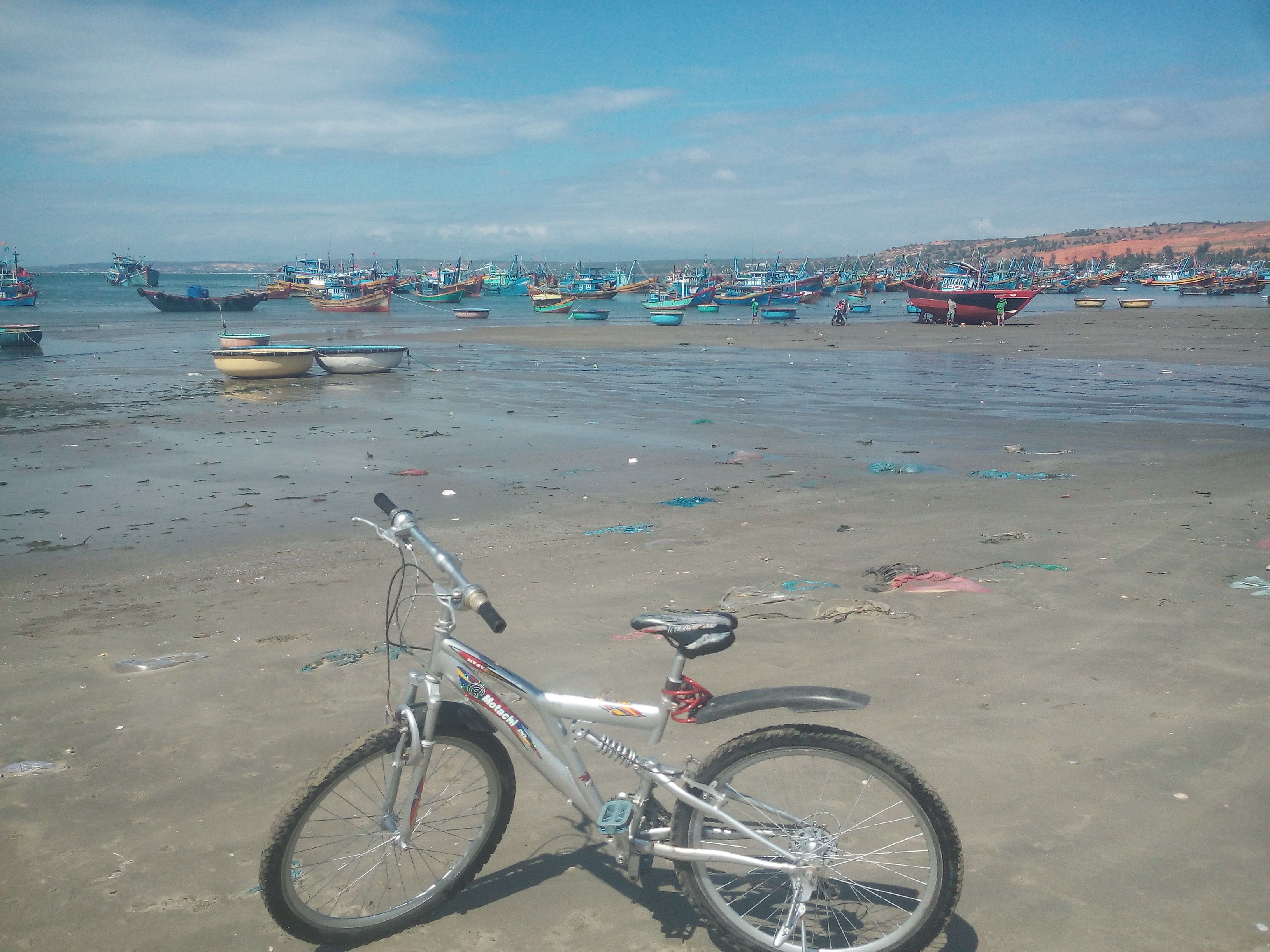 A bicycle parked on a sandy beach with boats in the background.