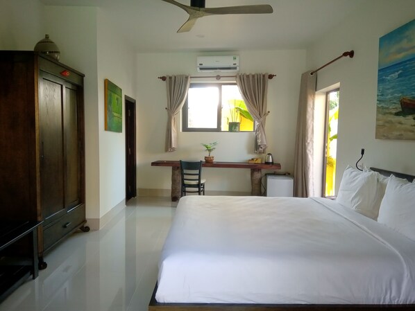 Una habitación de hotel con cama, escritorio, silla, aire acondicionado y ventana con cortinas.