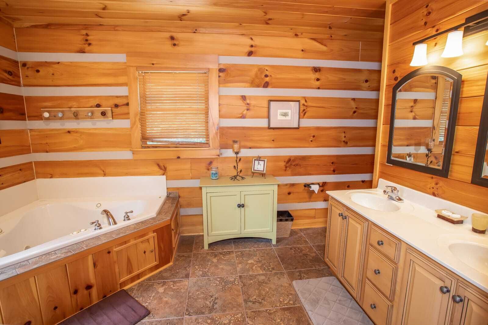 A log cabin bathroom with a large bathtub, two sinks, a vanity, and a mirror.