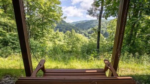 Een houten schommelbank met uitzicht op een bebost dal en bergen.