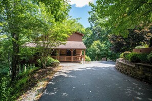 A lodge with a covered porch, surrounded by dense greenery and a stone retaining wall.