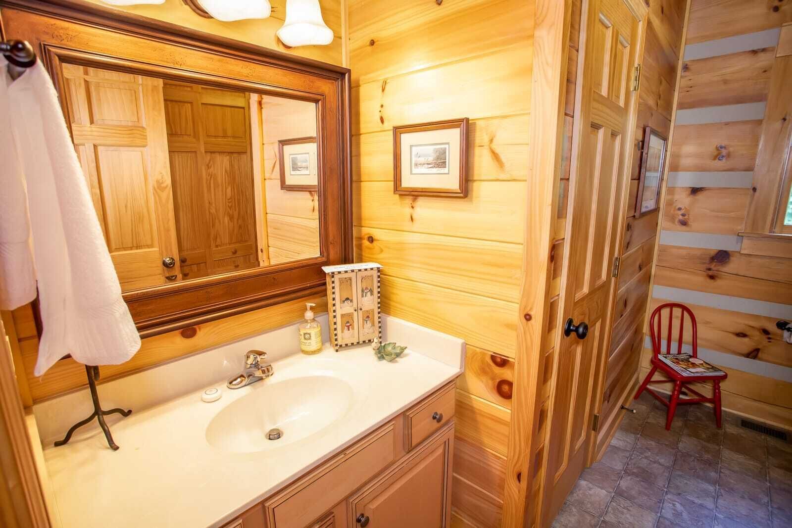 Une salle de bain rustique, aménagée dans une cabane en bois, avec un grand miroir, un lavabo et un petit meuble où sont posées des photos.