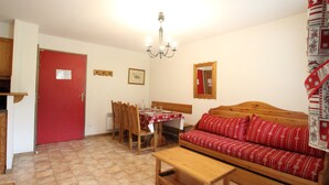 A cozy living room with a wooden sofa, a dining table, and a red door. - Spacious apartment for 6 people at the foot of the slopes with parking and WIFI (Lanslevillard)