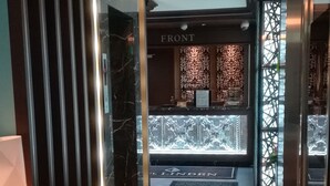 A modern hotel lobby with a patterned carpet, a reception desk labeled "FRONT," and a decorative wall with a geometric pattern. - Hotel Linden Oji (Tokyo)
