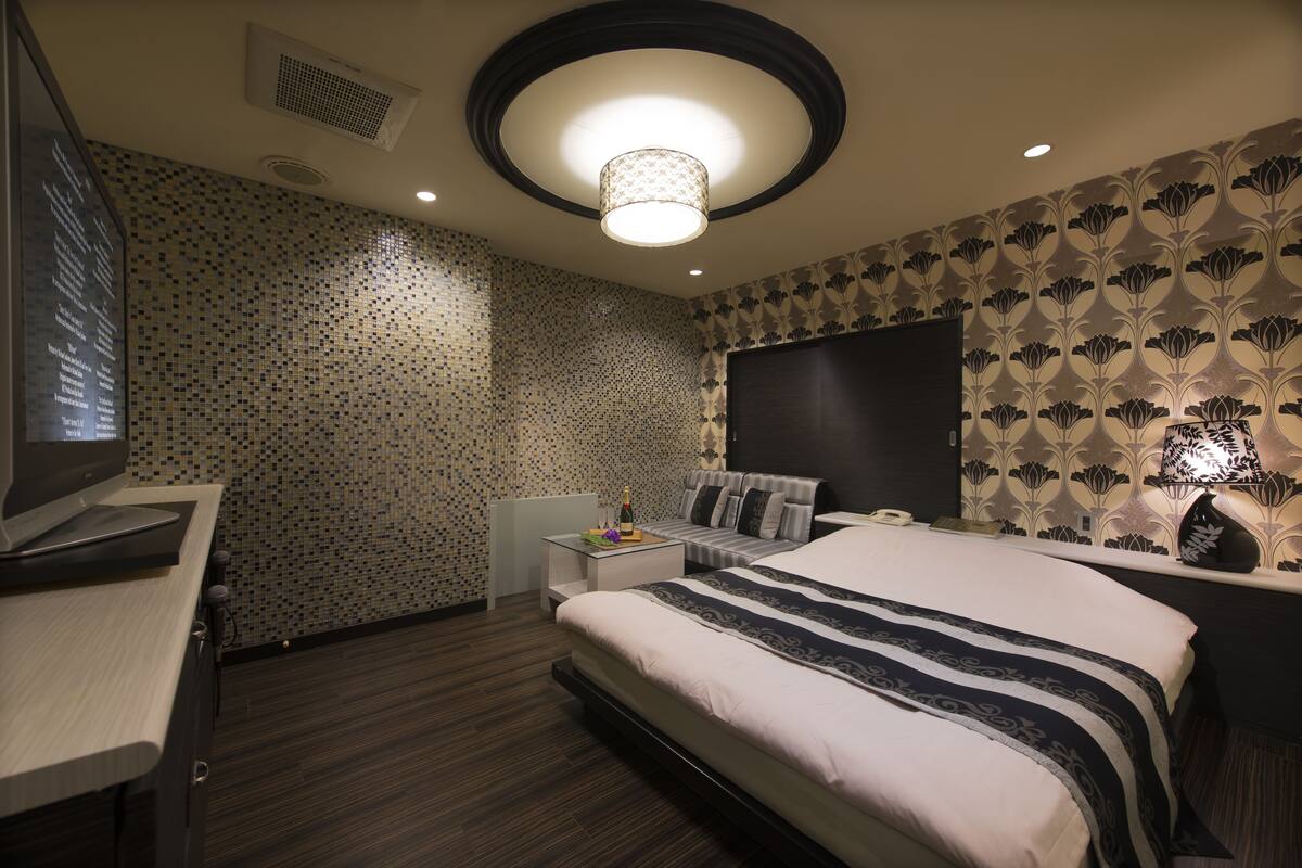 A modern hotel room with a large bed, a desk with a computer, a TV, and a wall-mounted heater.