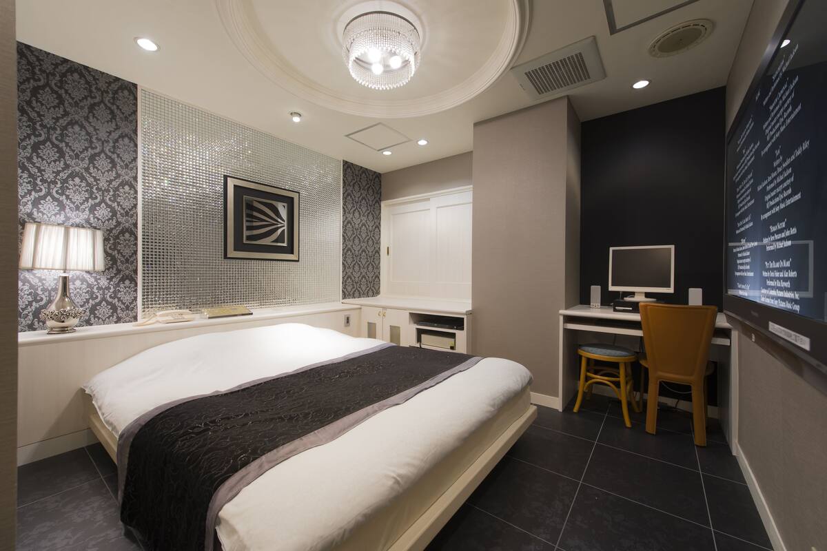 A hotel room with a large bed, a desk with a computer, and a wall-mounted TV.