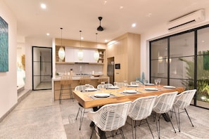 A modern kitchen with a central island, pendant lighting, and a dining area with a wooden table and white chairs.
