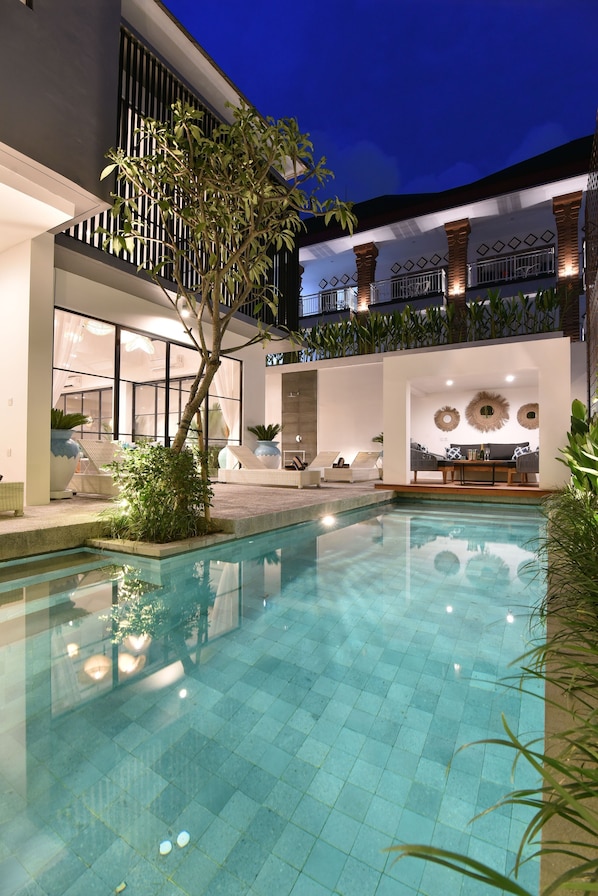 A modern outdoor pool area with a clear blue pool, lounge chairs, and a dining area with a table and chairs.