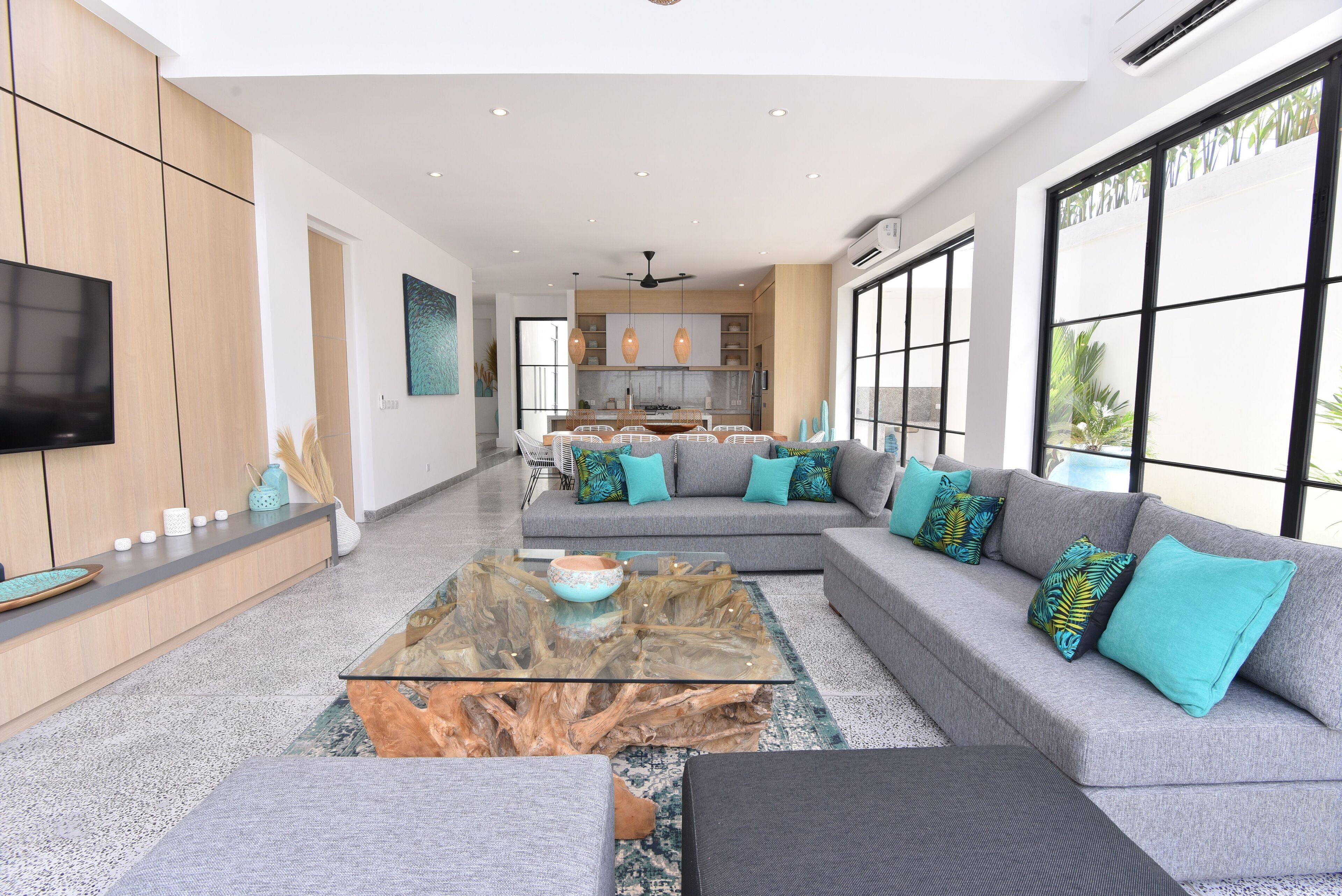 A modern living room with a grey sectional sofa, a glass coffee table, and a flat-screen TV mounted on the wall.