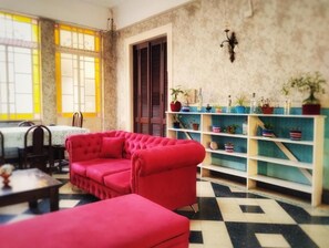 Een kamer met een rode bank, een eettafel met stoelen, een boekenkast met planten en een vloer met een patroon.