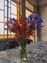 Una mesa con mantel estampado de periódico, un florero con flores y una ventana con marco decorativo.