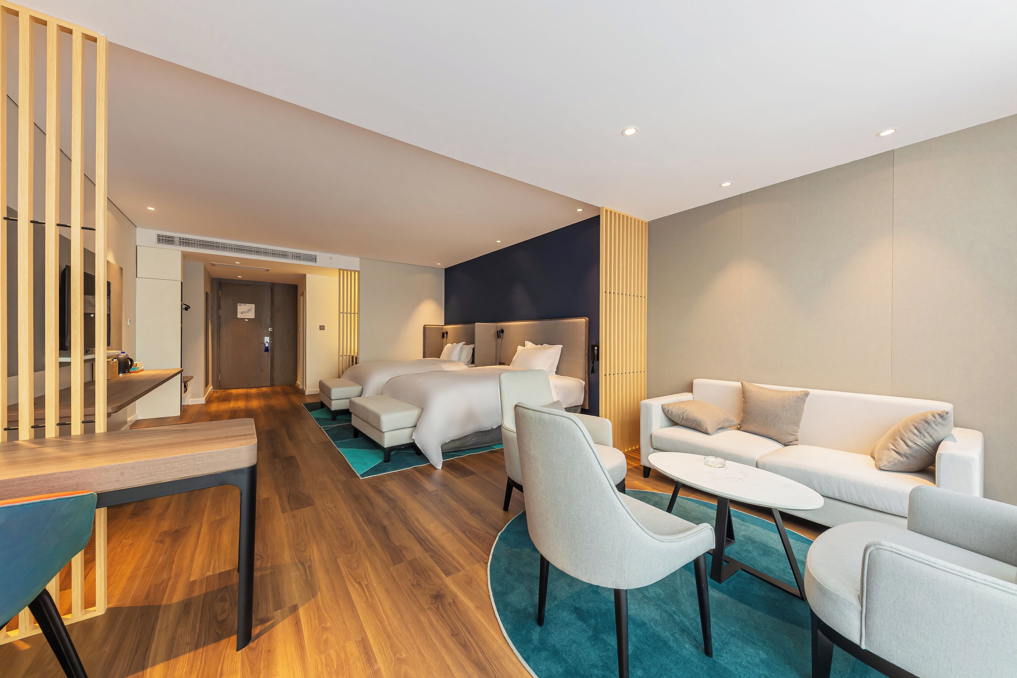 A modern hotel room with a wooden staircase, a sofa set, a dining table, and a bed with a headboard.