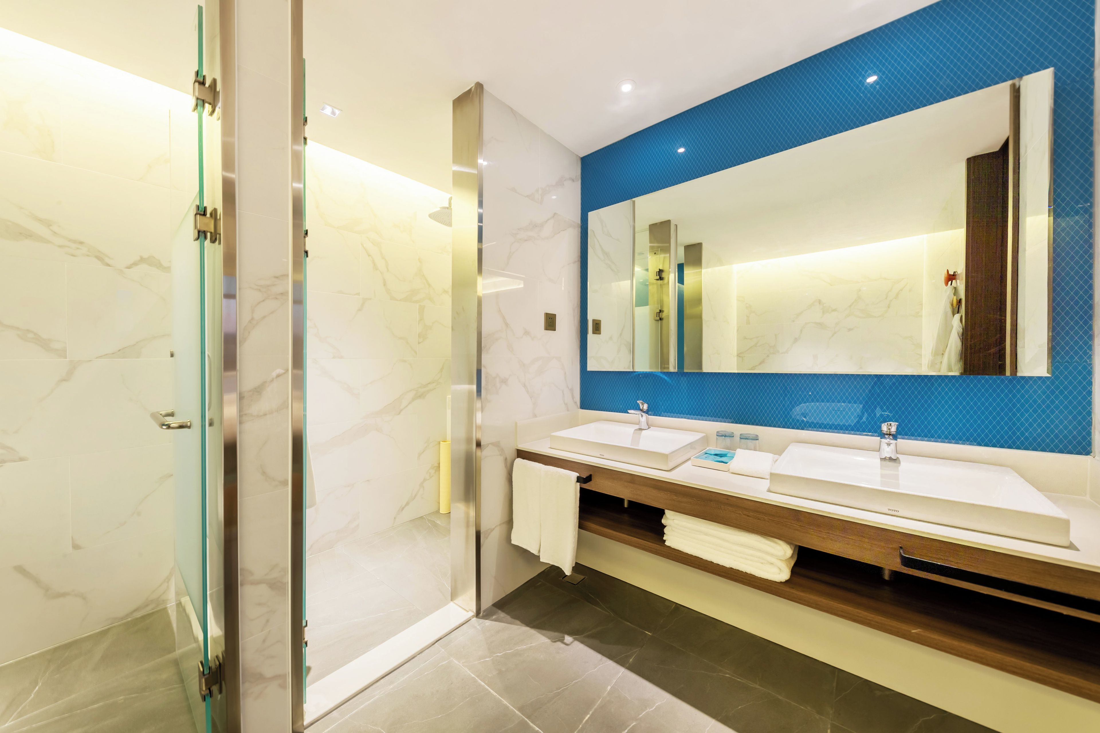 A modern bathroom with two sinks, a large mirror, and a glass shower enclosure.