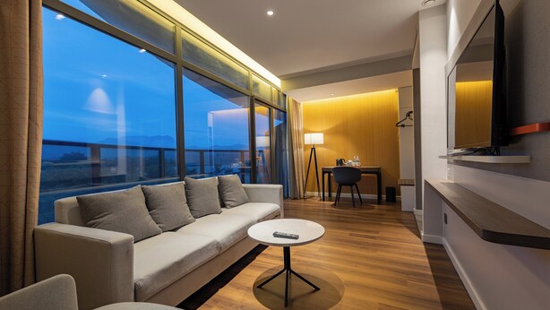A modern hotel room with a sofa, a small round table, a TV, and a large window offering a city view. - Holiday Inn Express Yichang Riverside by IHG (Yichang)
