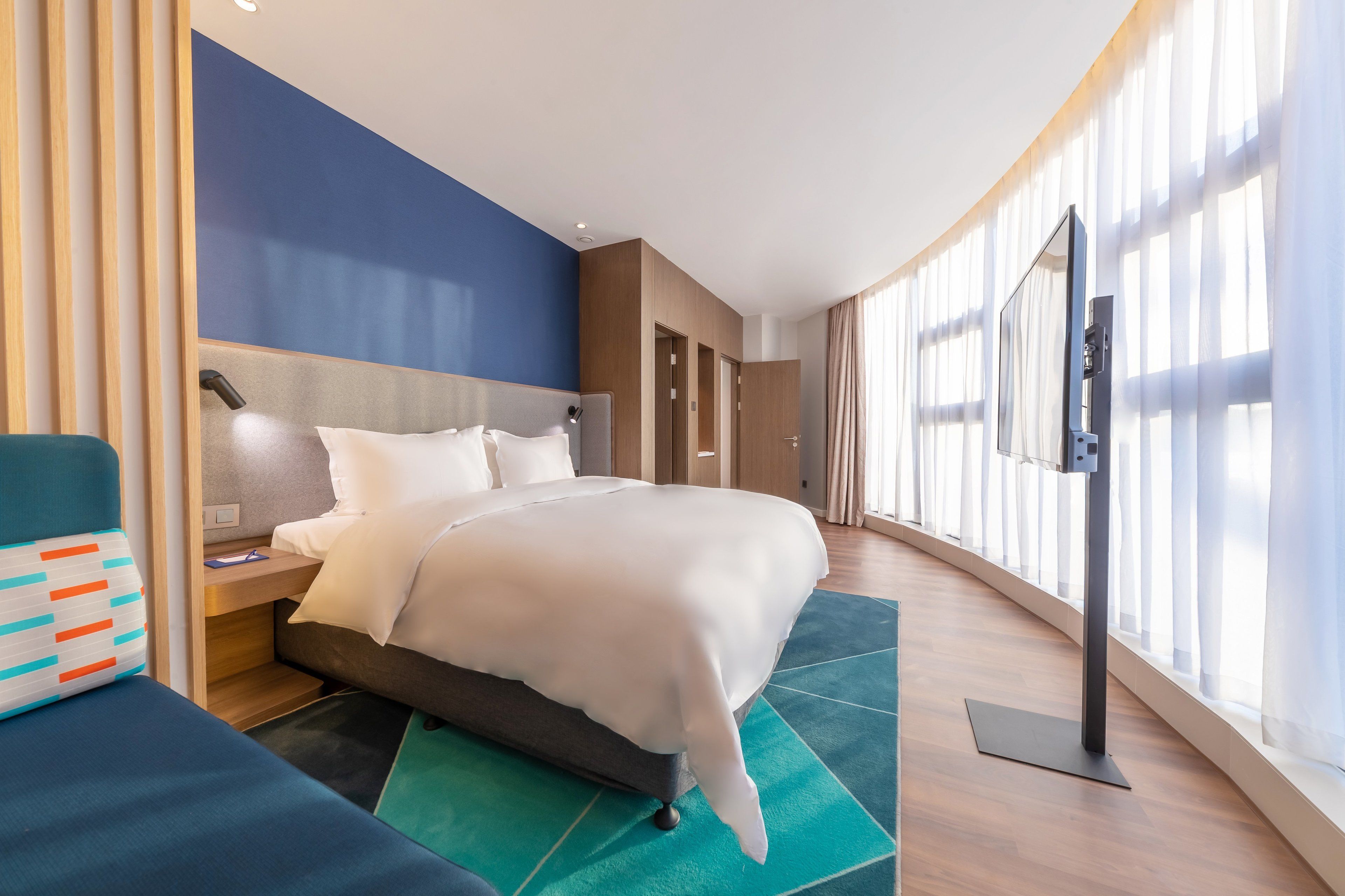 Ett modernt hotellrum med en stor säng, ett skrivbord, en stol och en TV.