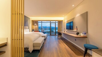 Habitación de hotel con una cama grande, un escritorio con televisor y vistas a las montañas.