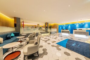 A modern lobby with seating areas, a reception desk, and a staircase leading to upper floors.