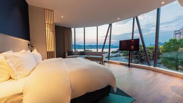 Una habitación de hotel moderna con una cama grande, zona de estar y vistas a un puente y el paisaje urbano.