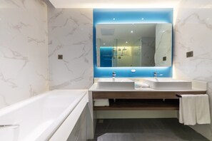 A modern bathroom with two sinks, a large mirror, and a bathtub.