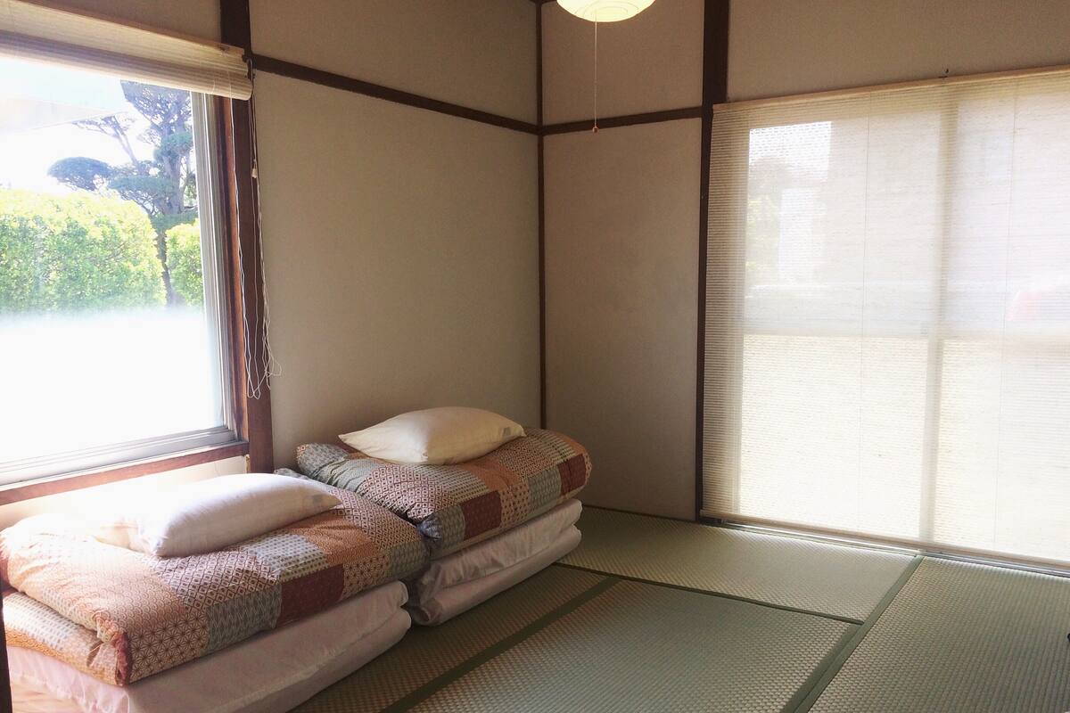 Quarto japonês tradicional com tatames, uma cama baixa com roupa de cama estampada e um painel deslizante shoji.